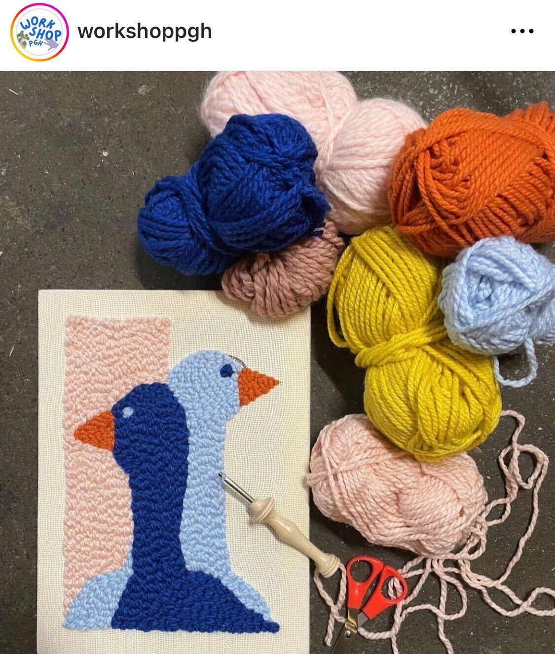 A pile of colored yarn next to a cross stitch artwork of two ducks.