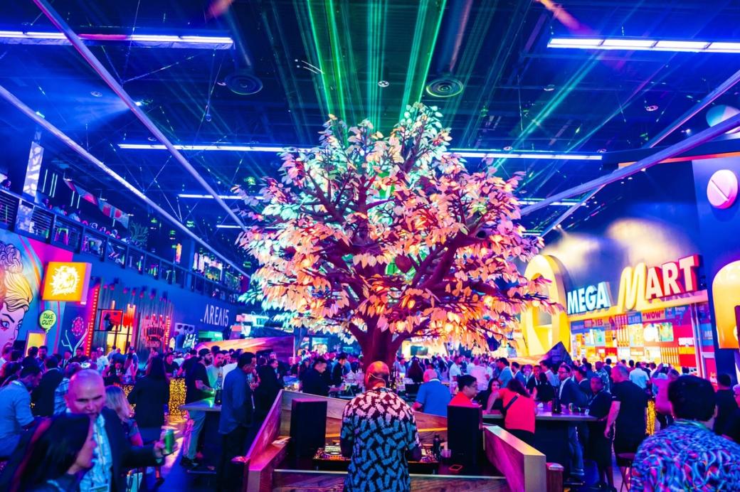 People gather around a tree with neon lights for leaves at AREA15.