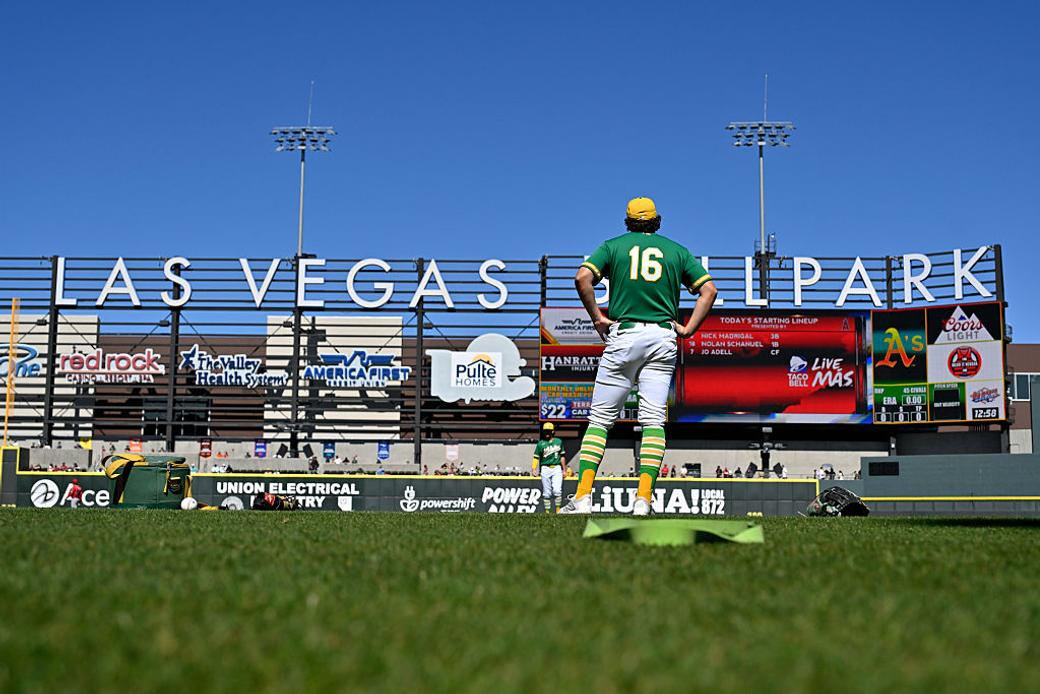 An Oakland A's baseball player wearing jersey number 16 stands on the field looking at the Las Vegas Ballpark outfield wall and scoreboard.