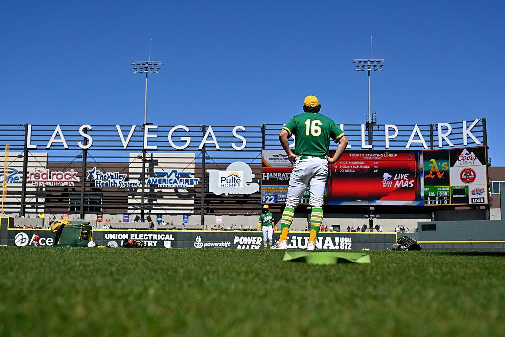 An Oakland A's baseball player wearing jersey number 16 stands on the field looking at the Las Vegas Ballpark outfield wall and scoreboard.