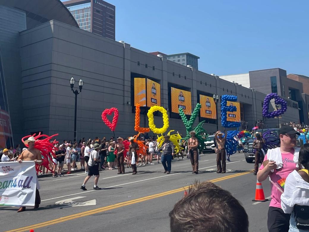 People marching in a parade holding letters made from balloons that spell LOVE.
