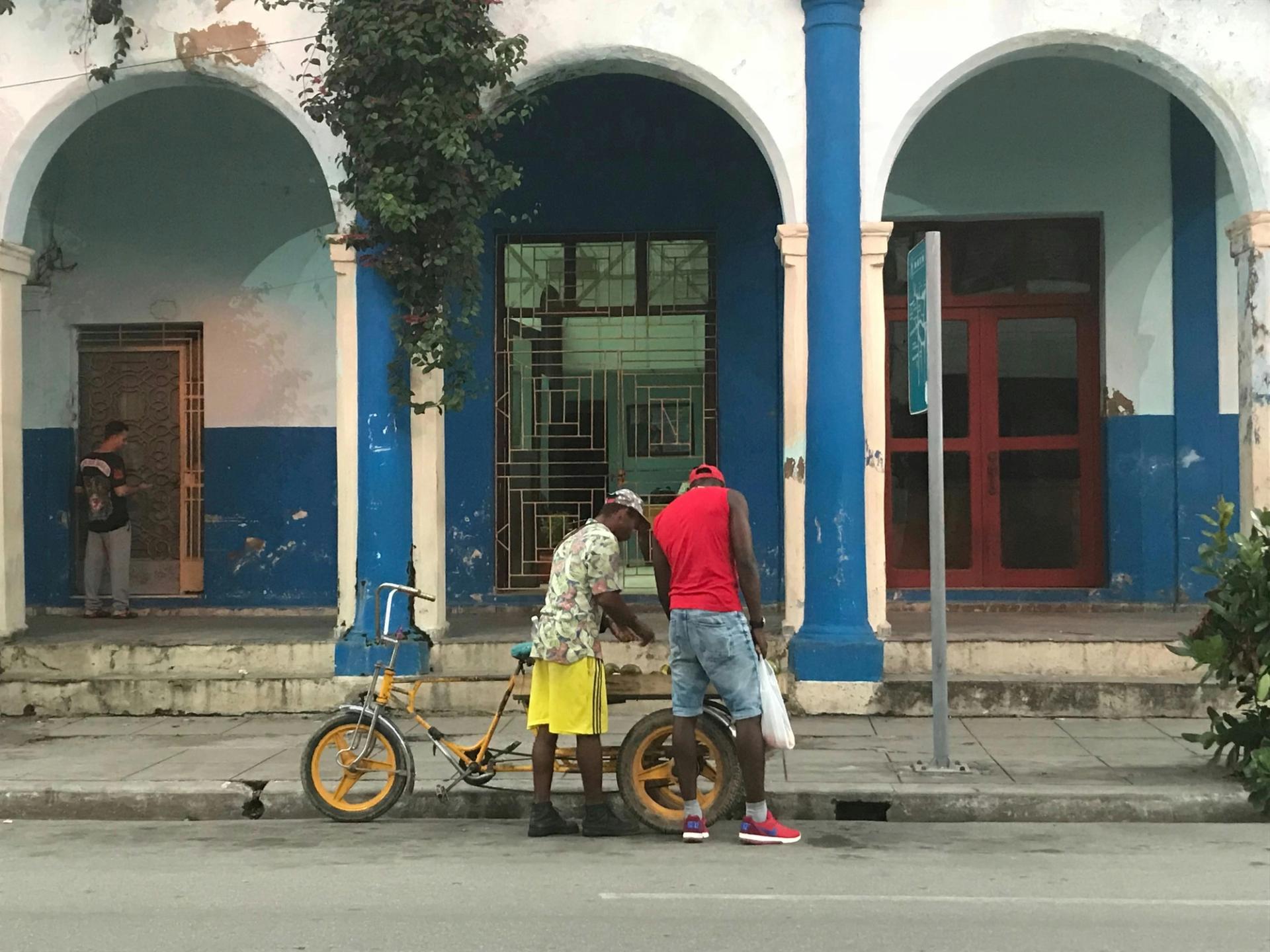 A man talks to another man on a bicycle on a city street.