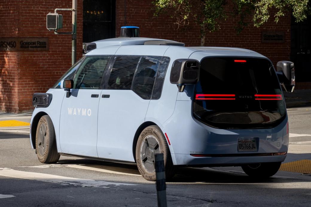 A blue Waymo van stops at an intersection 