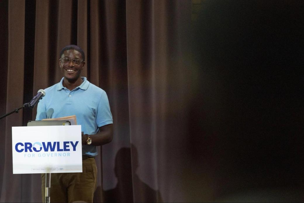Governor candidate David Crowley stands at a podium with a campaign sign.