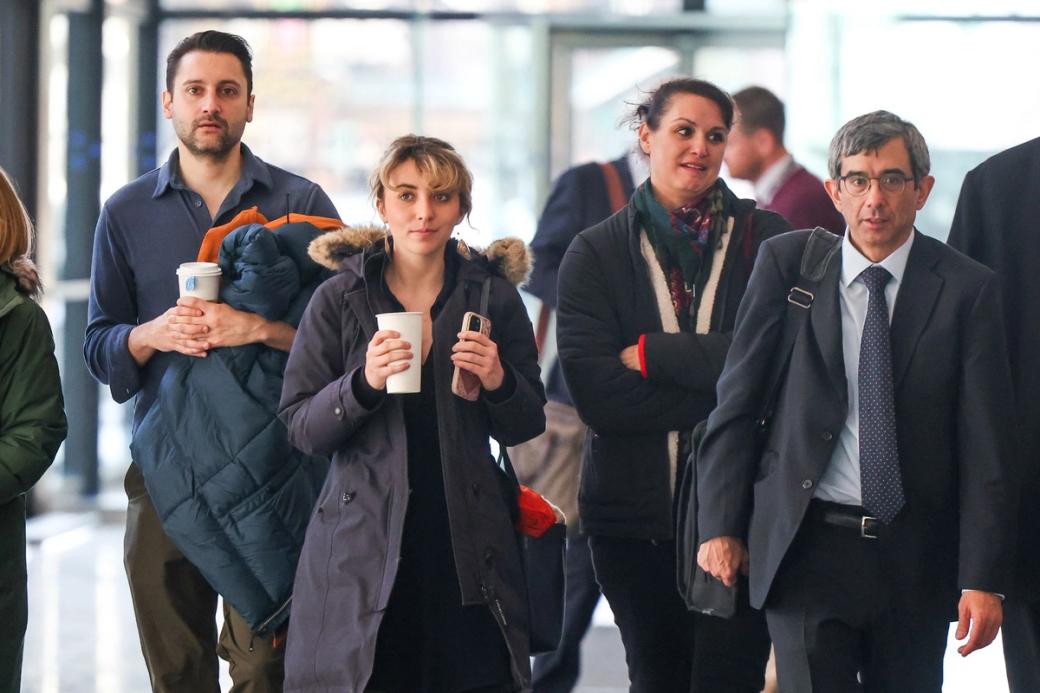 A group of people walking, two of which have coffees in their hands