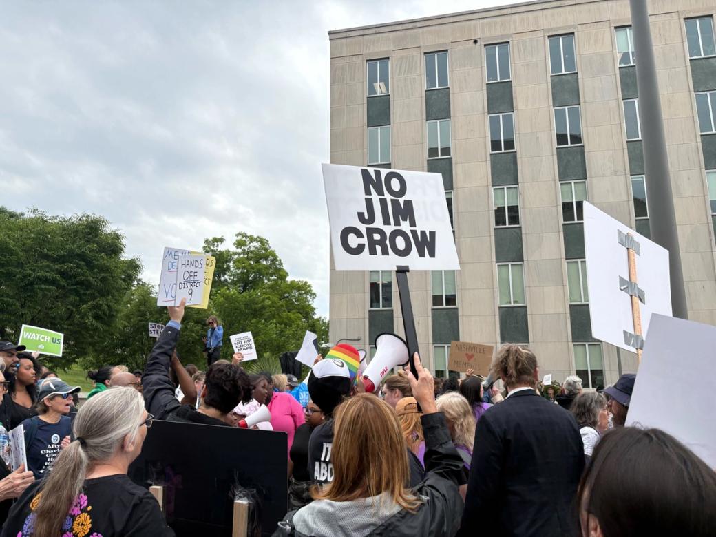 Protestors with signs, one reading "No Jim Crow," gather outside a building.