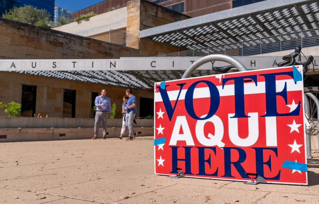 A red sign that says "Vote aquie here" outside Austin City Hall.