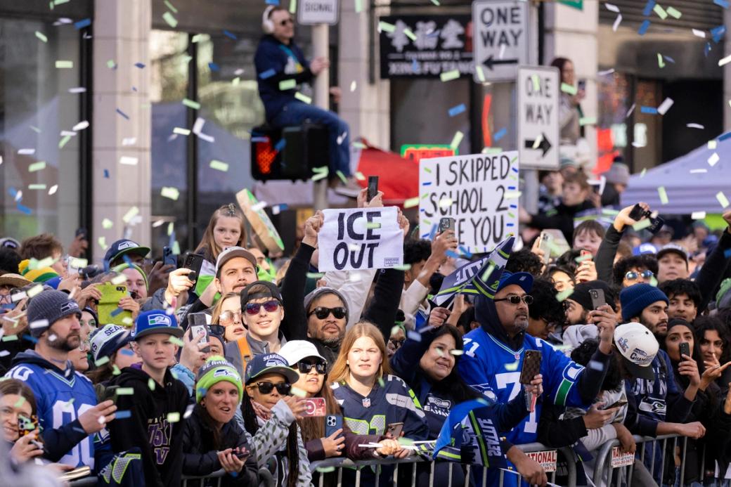 A photo of many Seahawks fans wearing hats, jerseys, and holding up signs. One sign reads ‘ICE OUT’