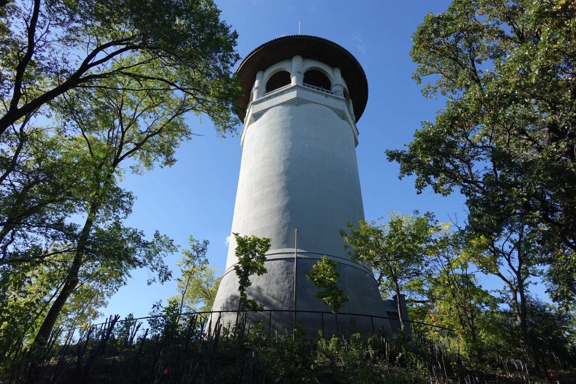 A large old white water tower in the center of a lightly forested area