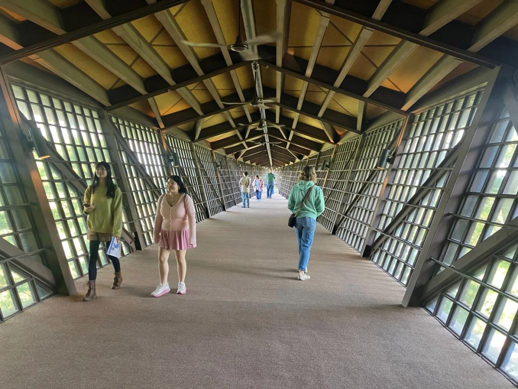 People walk through a long carpeted hallway with an arched ceiling and walls of small windows.
