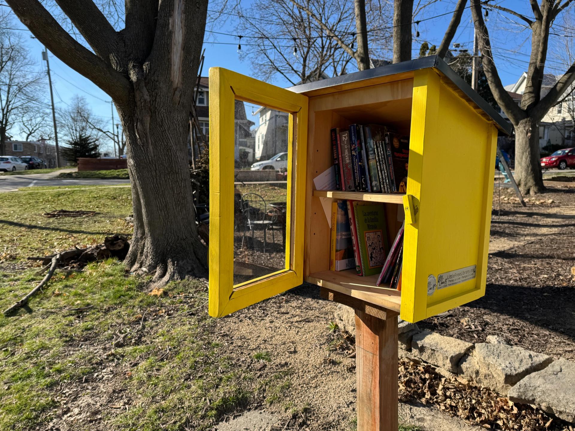 A yellow little free library is shown on a sunny day