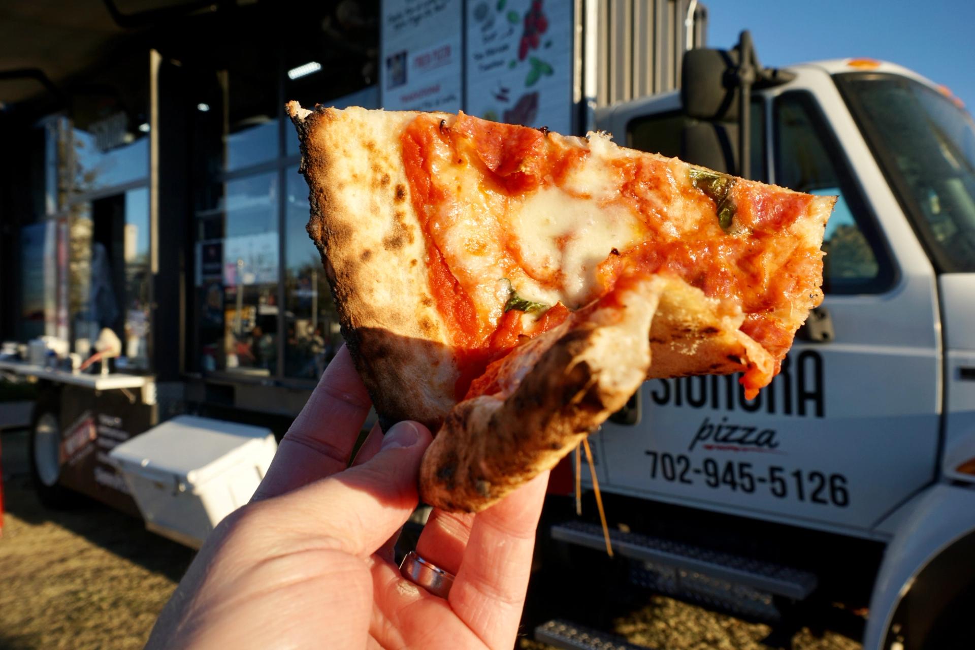 A slice of pizza in front of a food truck.