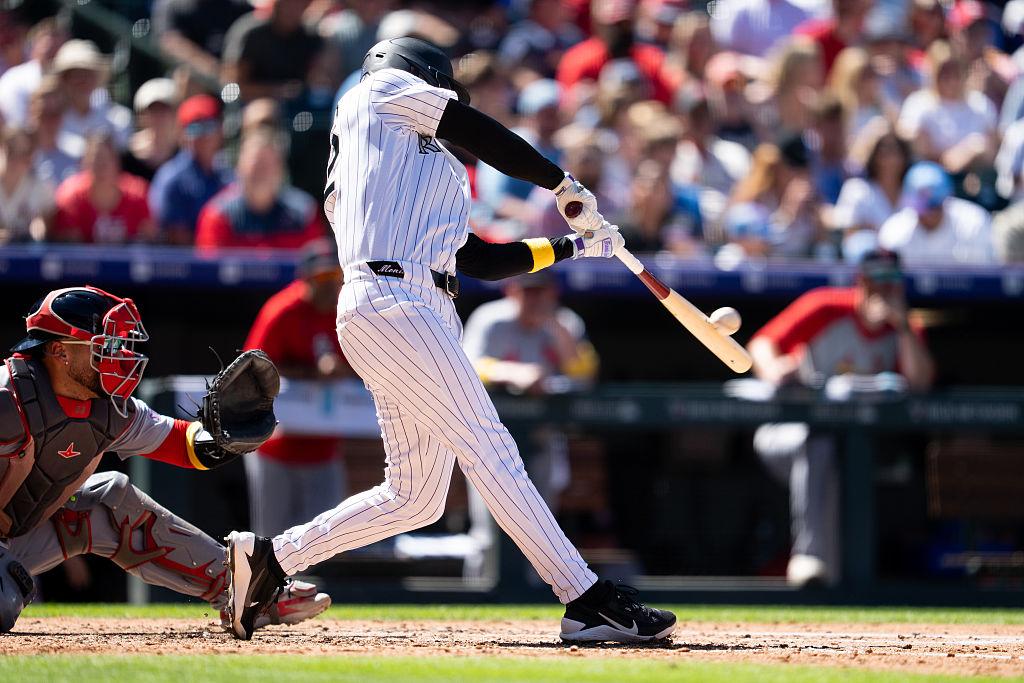 Baseball player swings bat against ball with crowd in the background