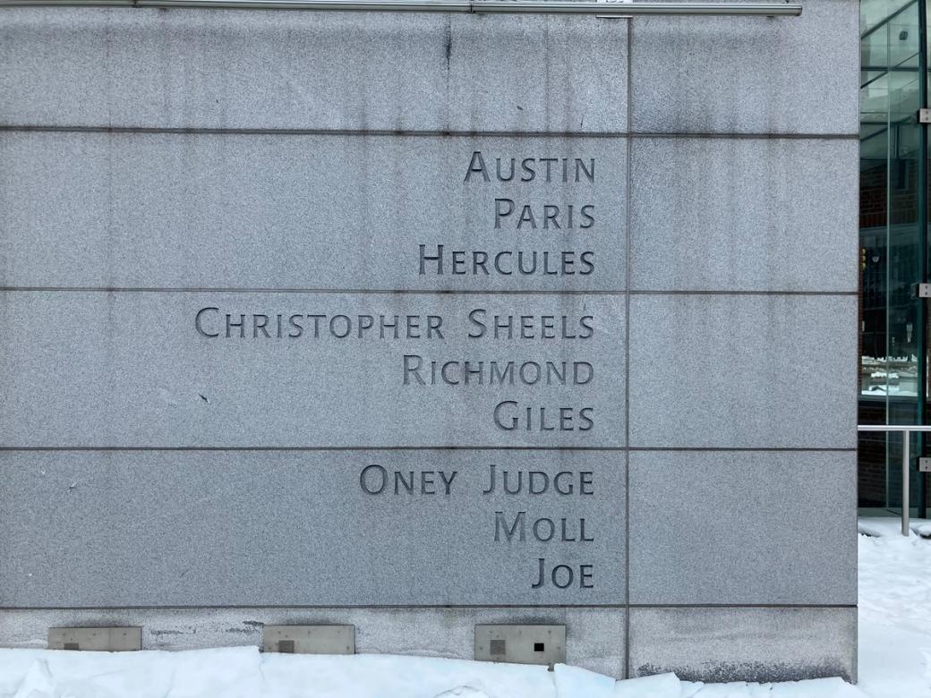 Names etched into a stone wall: Austin, Paris, Hercules, Christopher Sheels, Richmond, Giles, Oney Judge, Moll, Joe