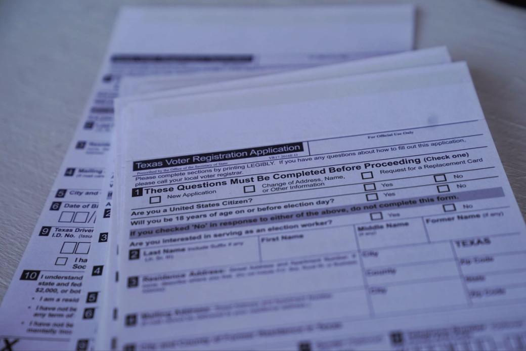 stacks of white paper with the title "Texas Voter Registration Application"