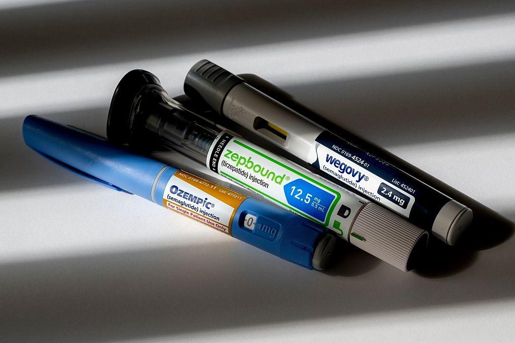 Three injectable GLP-1 medication pens labeled Ozempic, Zepbound, and Wegovy lie on a gray surface.