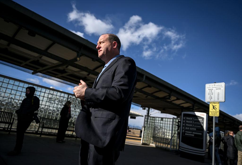 Polis stands outside an RTD light rail stop in 2024