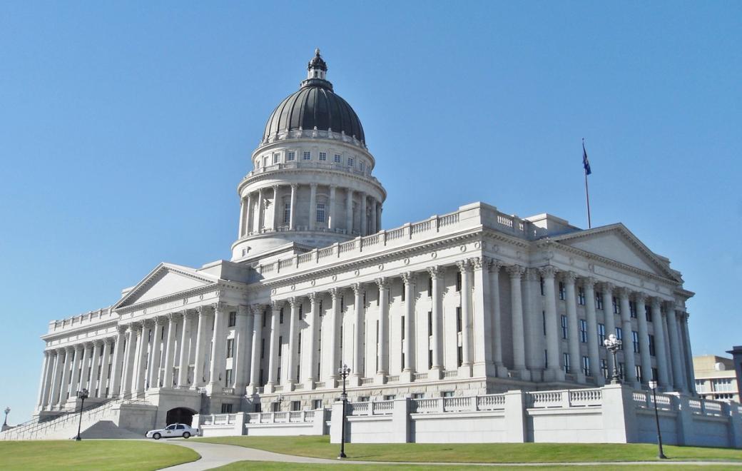 The Utah State Capitol, a white neoclassical building with a large dome and columns, under a clear blue sky.