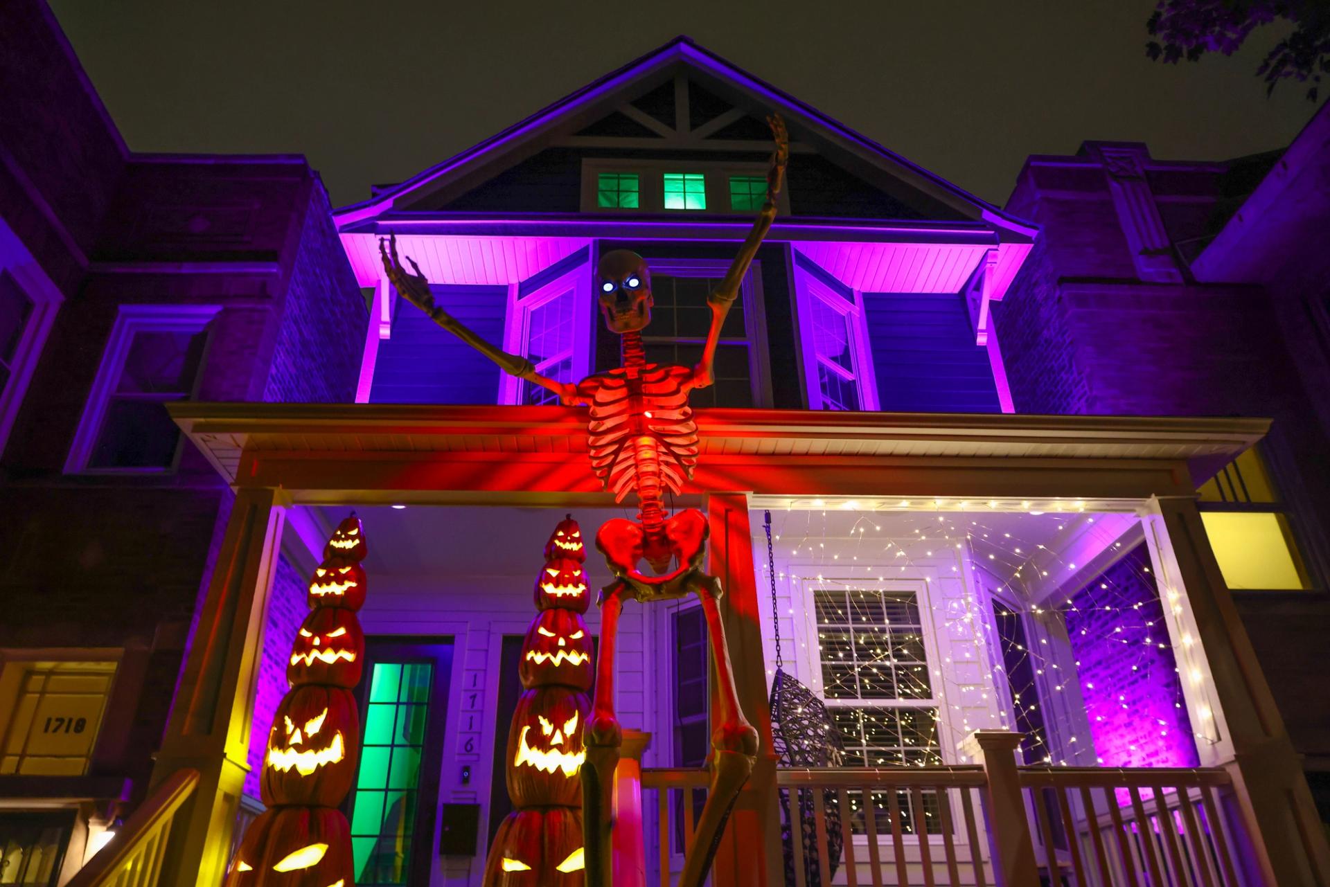 A large skeleton decoration reaching up in front of a purple lit home with other halloween decorations