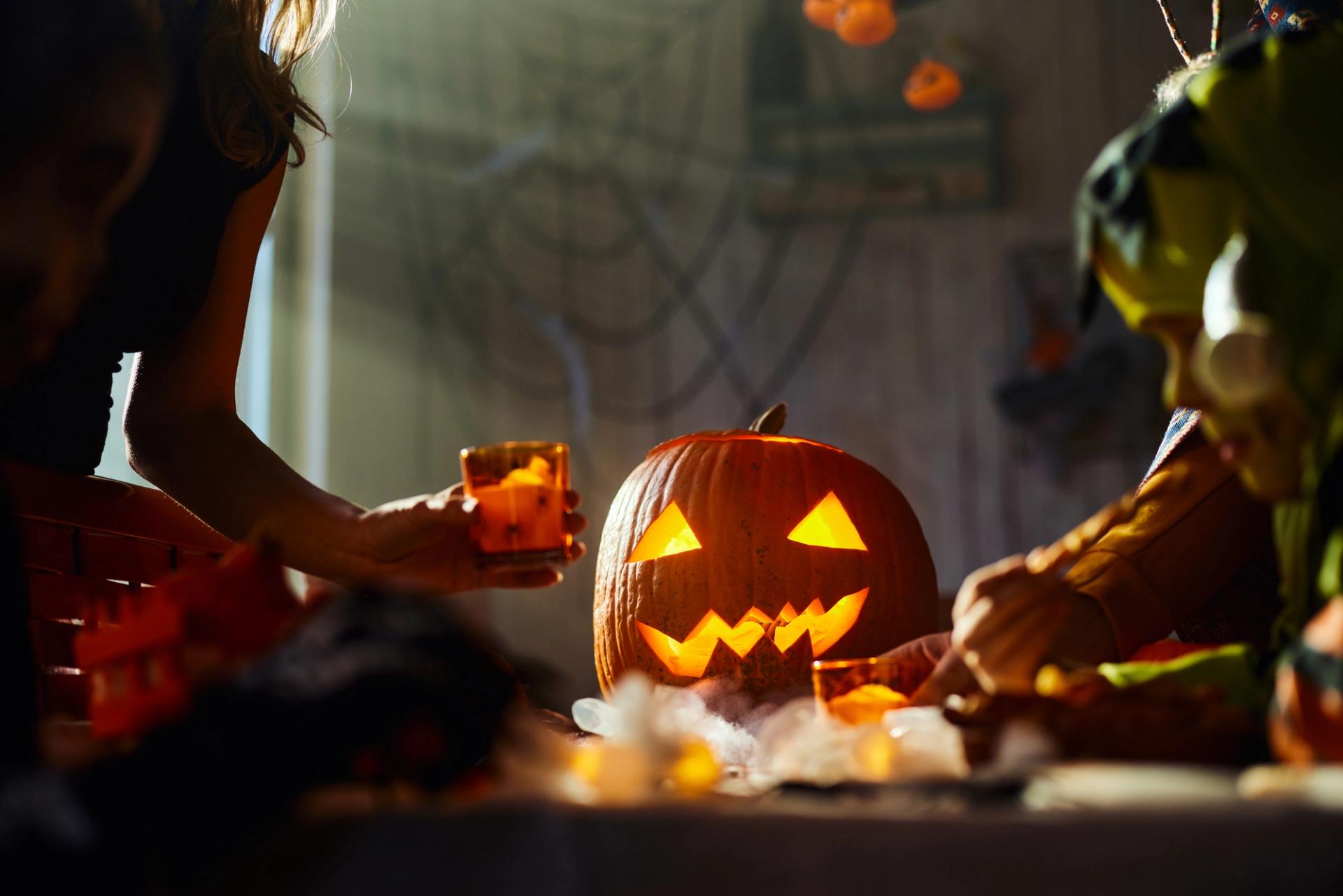 Two hands decorate a table with a carved pumpkin on it.