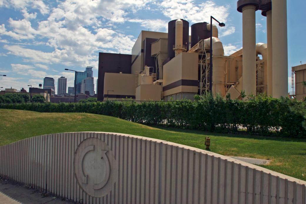 Large industrial building in foreground, and urban skyline with skyscrapers in background
