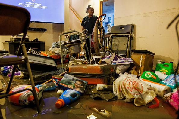 A person looks at a flooded basement littered with damaged items.