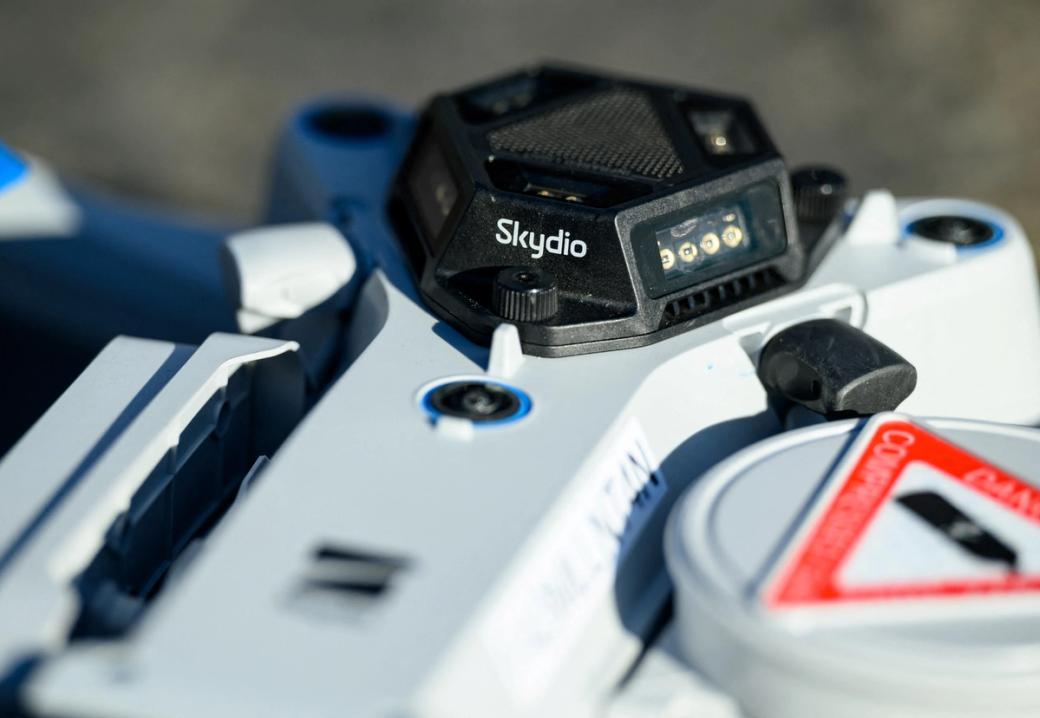 A close up of a white, blue, and black drone with the name of the company “Skydio.”