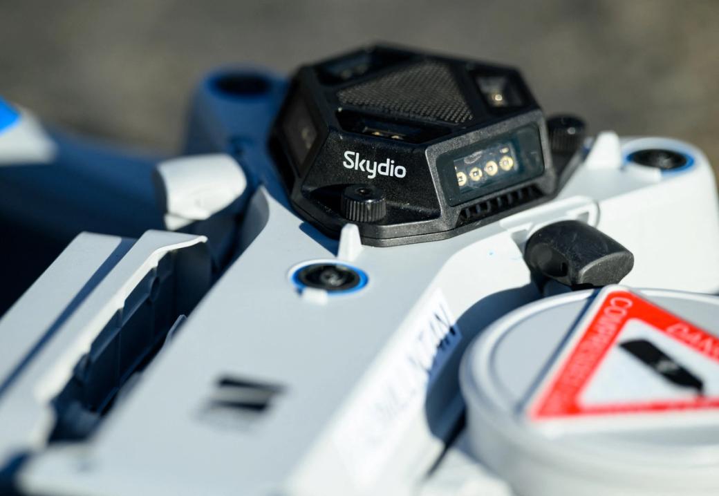 A close up of a white, blue, and black drone with the name of the company “Skydio.”