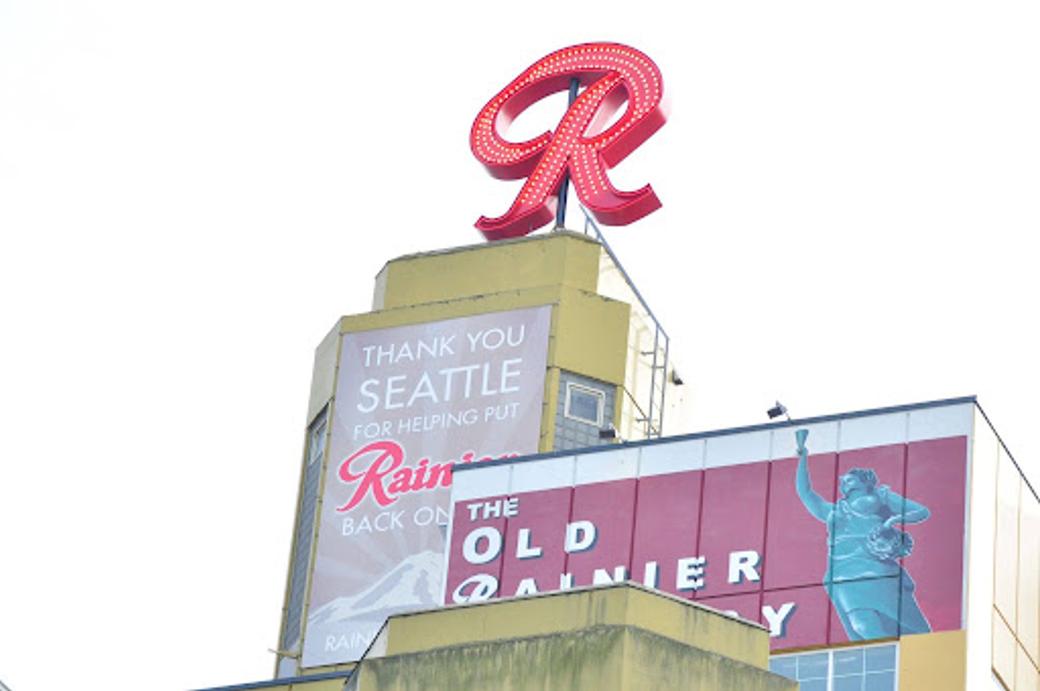 The red, light up Rainier R sits refreshed atop the Old Rainier Brewery building with its faded yellow/gold paint and Rainier Brewery signage.