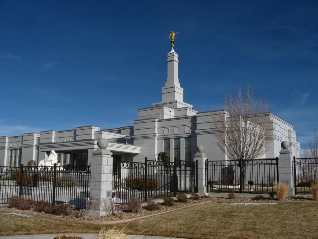 A white Church of Jesus Christ of Latter-day Saints temple behind a black gate on a sunny day. 