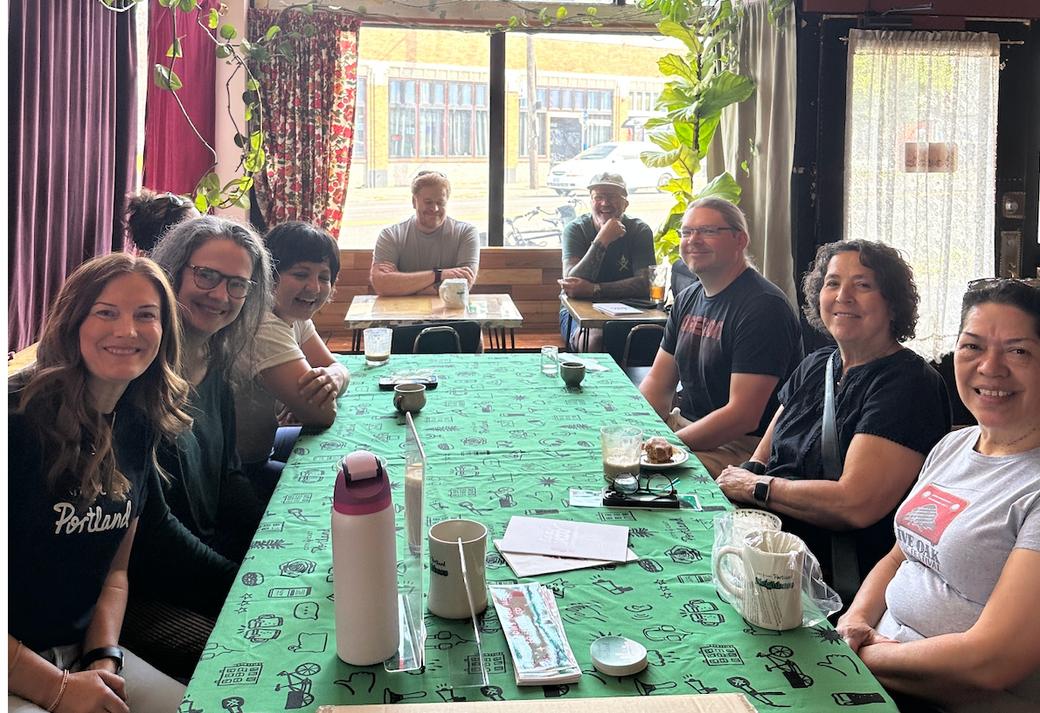 Group of adults sitting at long rectangle table inside restaurant, smiling at camera