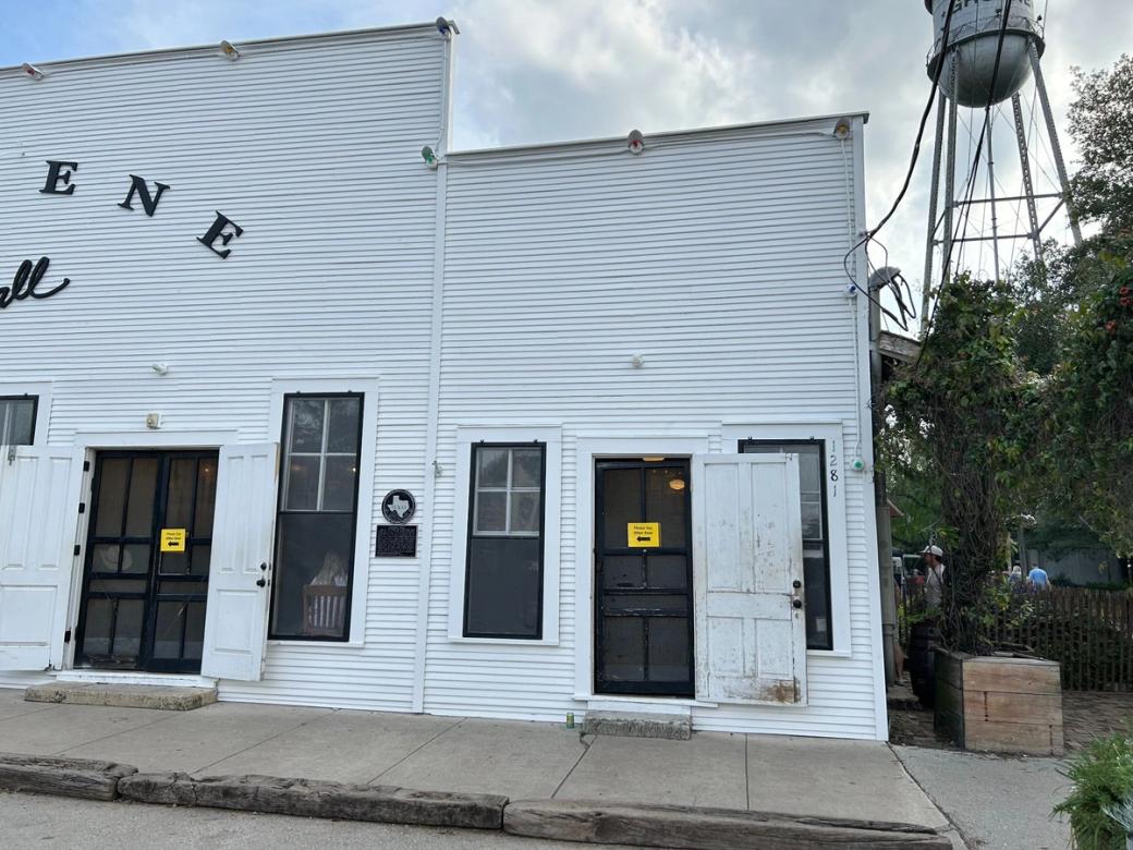 A white building with several black screen doors and windows. The name of the building is cut off except for "ENE." A water tower is in the back right.
