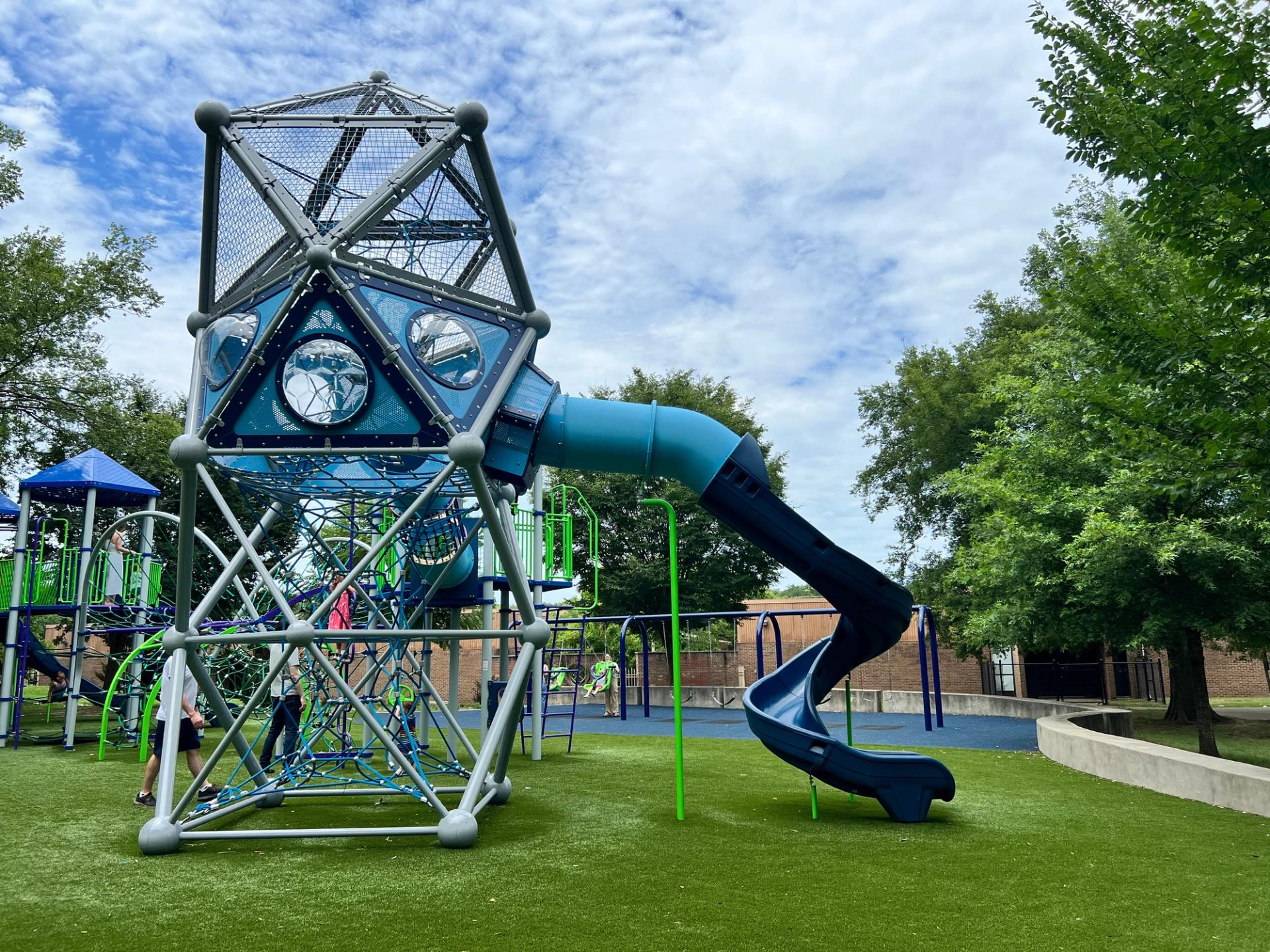 A large blue climbing structure made of ropes, with a blue twisty slide at the top.