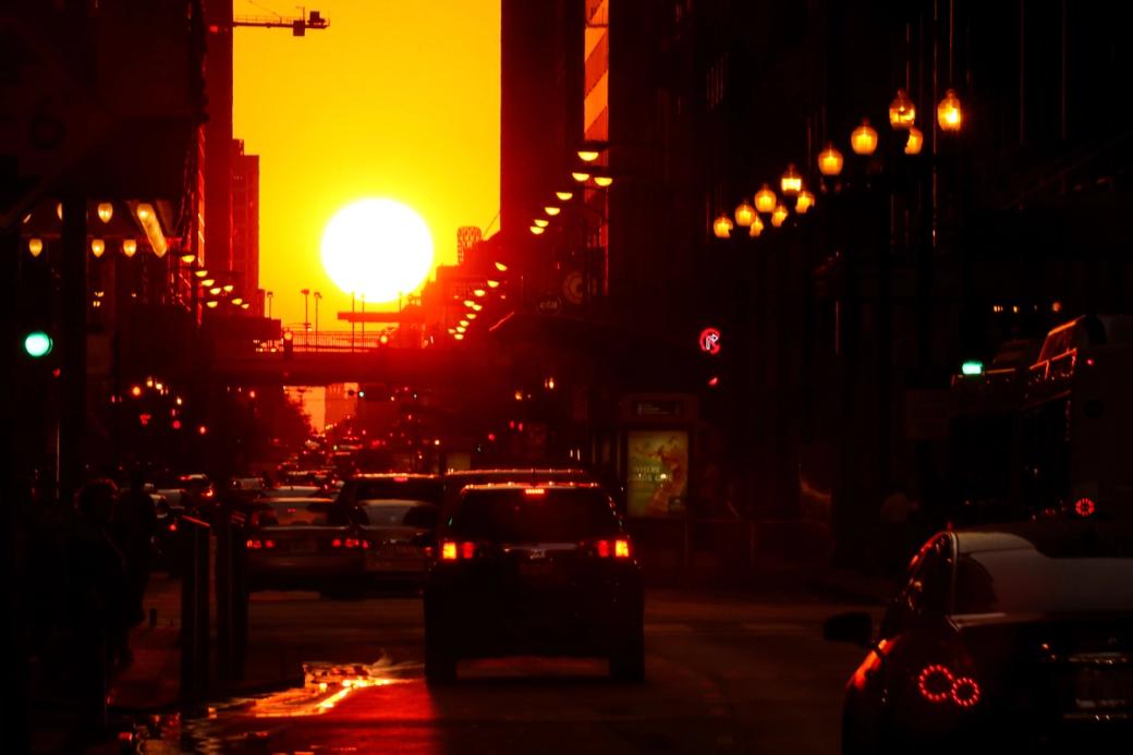 View of sunset from urban street level, with many cars driving towards the setting sun