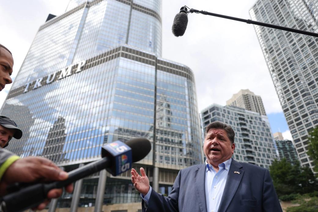Governor of Illinois JB Pritzker in a blue suit speaking to reporters with mics in front of Trump tower.