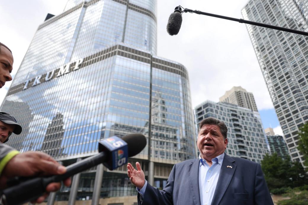 Governor of Illinois JB Pritzker in a blue suit speaking to reporters with mics in front of Trump tower.