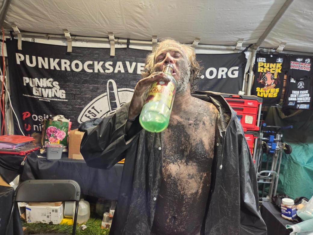 A man covered in mud drinking a green drink out of a bottle