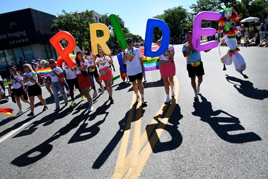 Parade participants hold up colorful balloons spelling "PRIDE"