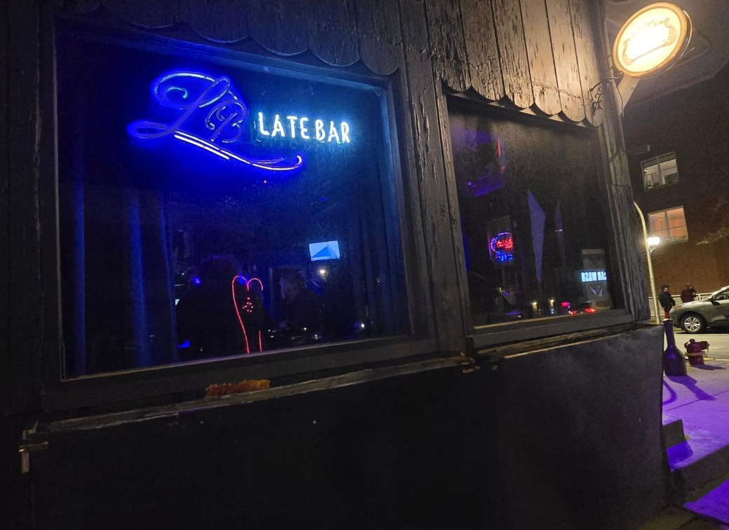 The outside of a bar with a neon light that says "late bar"