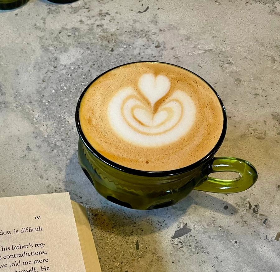 A latte in a green mug, the corner of an open book next to it.