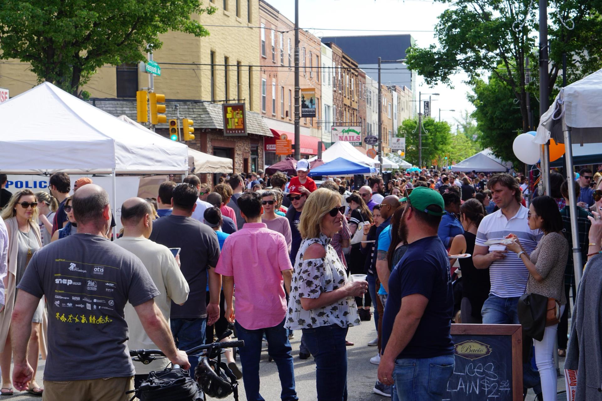 A crowd of people walking along a tent-lined street.