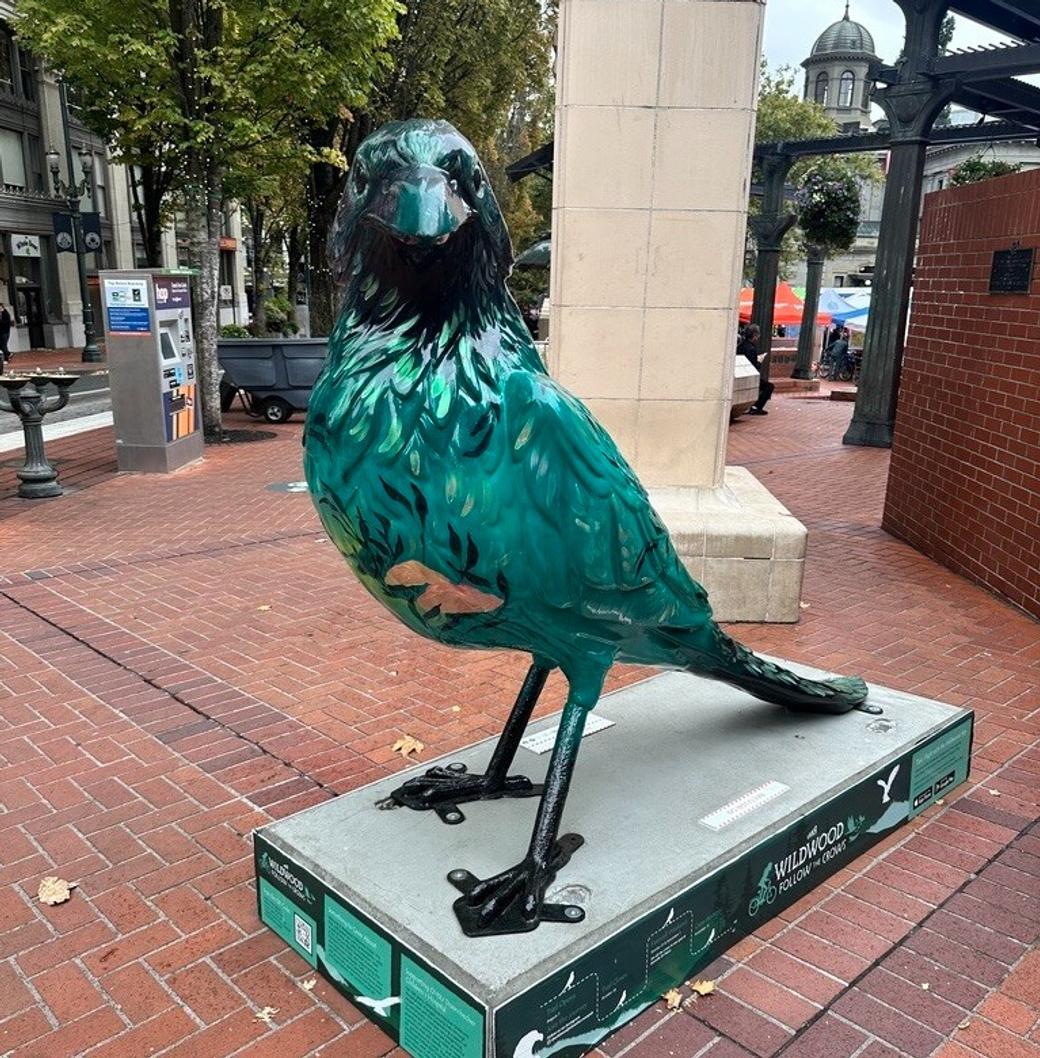 A large statue of a metallic turquoise and black crow in downtown Portland.