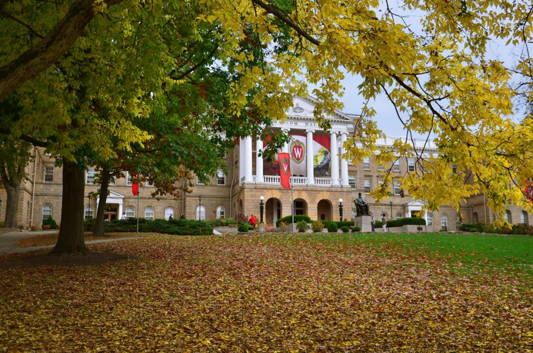 A building with white columns on a lawn strewn with leaves.