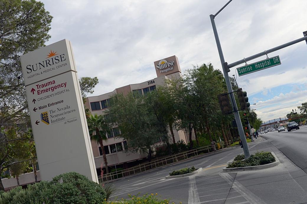 Exterior sign for Sunrise Hospital & Medical Center with directions to Trauma Emergency, next to a street sign for Sunrise Hospital DR.