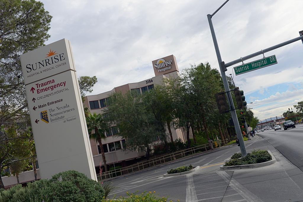 Exterior sign for Sunrise Hospital & Medical Center with directions to Trauma Emergency, next to a street sign for Sunrise Hospital DR.