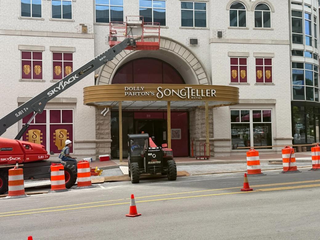 A white building with red currents in the windows with ST initials, and an awning that says Dolly Parton's SongTeller Hotel.
