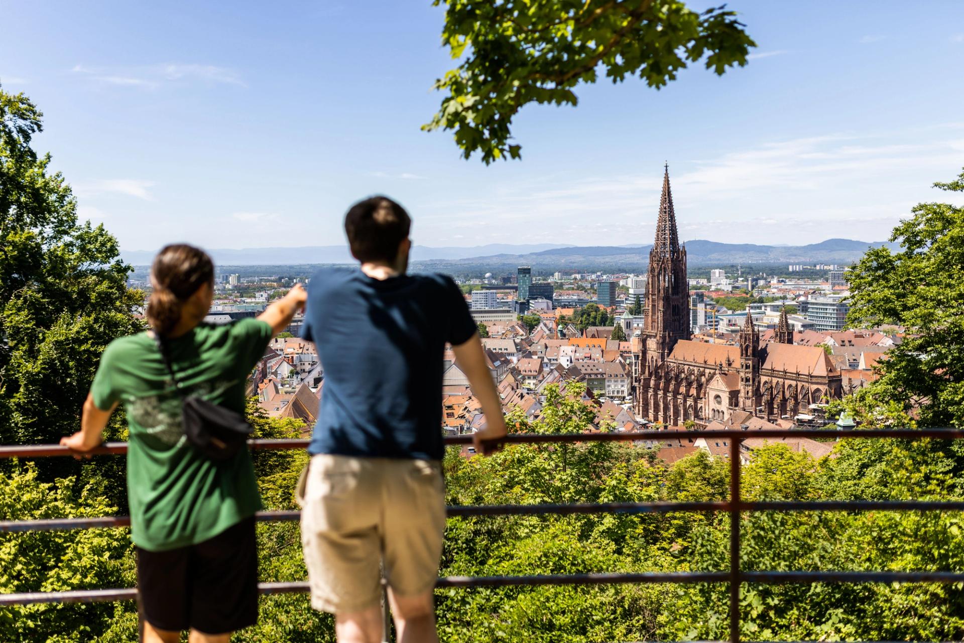 A man in a blue shirt and a woman in a green shirt look over a city.