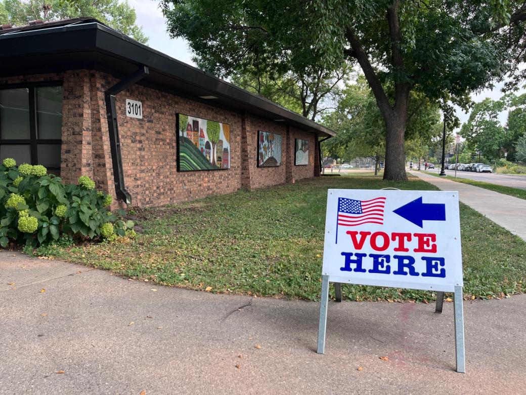 A sign that says "Vote Here" points to a polling place at a park.