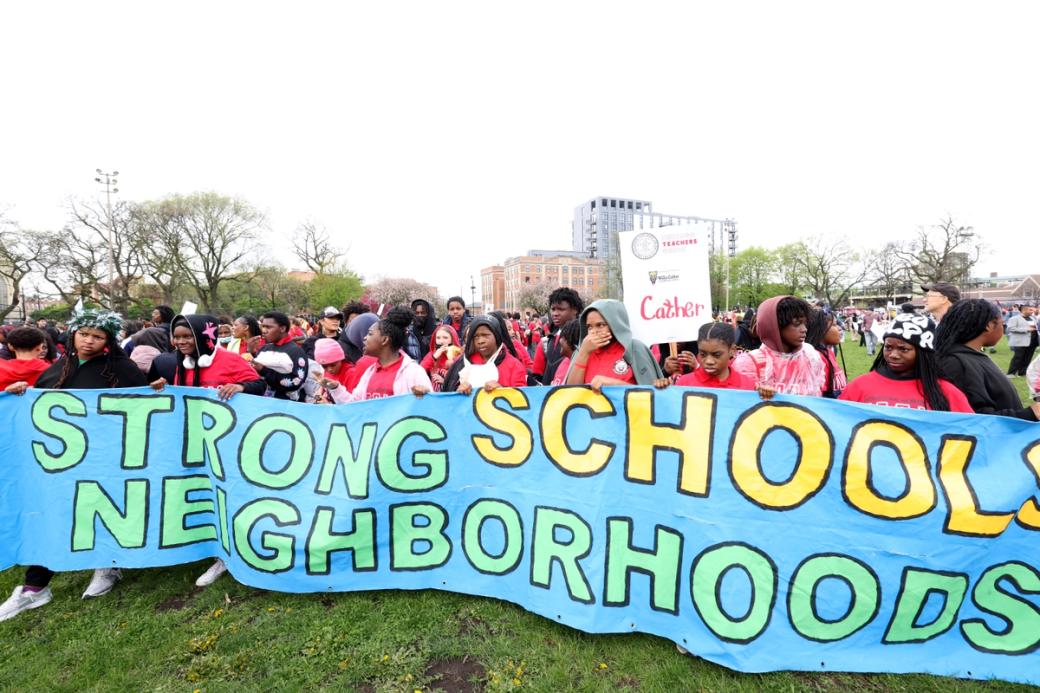 A group of people dressed in red holding up a sign. The sign reads "strong schools beighborhoods