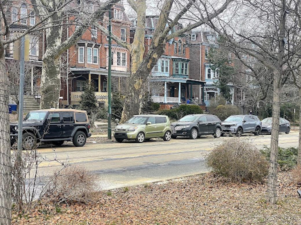  An image of colorful homes along West Philly's Baltimore Avenue. Multiple cars are parked along the street.